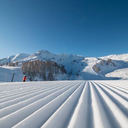 Frisch präparierte Piste mit Blick auf die höher liegende Pistenlandschaft und die schneebedeckte Umgebung