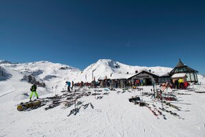 Gamskogelhütte mit vielen Skiern und Snowboards, Menschen genießen die Sonne, Bergpanorama