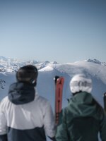 Zwei Skifahrer mit Skiern vor verschneiten Bergen und weitem Panorama in Zauchensee