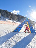Kind mit Ski fährt durch buntes Hindernis im Kinderland Zauchensee bei Sonnenschein