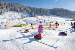 Kinder in Reifenkarussell auf Schneespielplatz mit Förderband und Parcours in Zauchensee