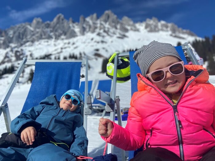 Children enjoying the winter sun in the mountains | © Anna Pilz Two children relaxing in lounge chairs with sunglasses in front of snowy mountains. | © Anna Pilz
