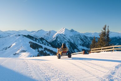 Person rides snow kart on freshly groomed slope with view of snowy mountains in bright sunshine. | © Dorfgasteiner Bergbahnen AG