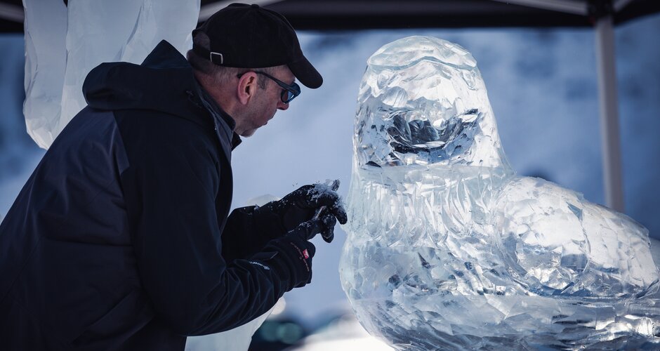 Ein Künstler arbeitet mit Handschuhen an einer detaillierten Eisskulptur in Form eines Vogels. | © TVB Dorfgastein, Max Steinbauer