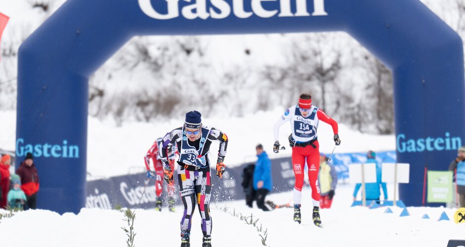 Langläufer kämpfen sich durchs Ziel bei den Gastein Classics | © Gasteinertal Tourismus, Mangotree Photography Zwei Langläufer im Zielsprint unter dem Gastein-Bogen, Schneespritzer fliegen durch die Luft. | © Gasteinertal Tourismus, Mangotree Photography