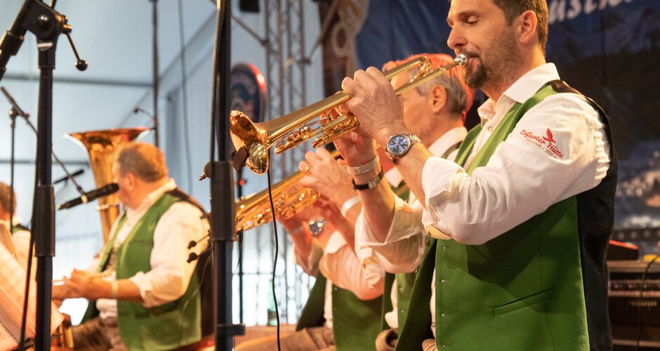 Der Flügelhornist der Musikgruppe "Innsbrucker Böhmischen" spielt gerade während man im Hintergrund zwei seiner Musikkollegen ebenfalls beim spielen sieht. | © Harald Steiner 