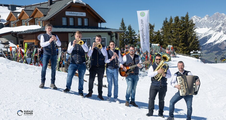 Sieben Musiker mit Instrumenten stehen im Schnee vor der Schladminger Hütte bei Sonnenschein | © Harald Steiner