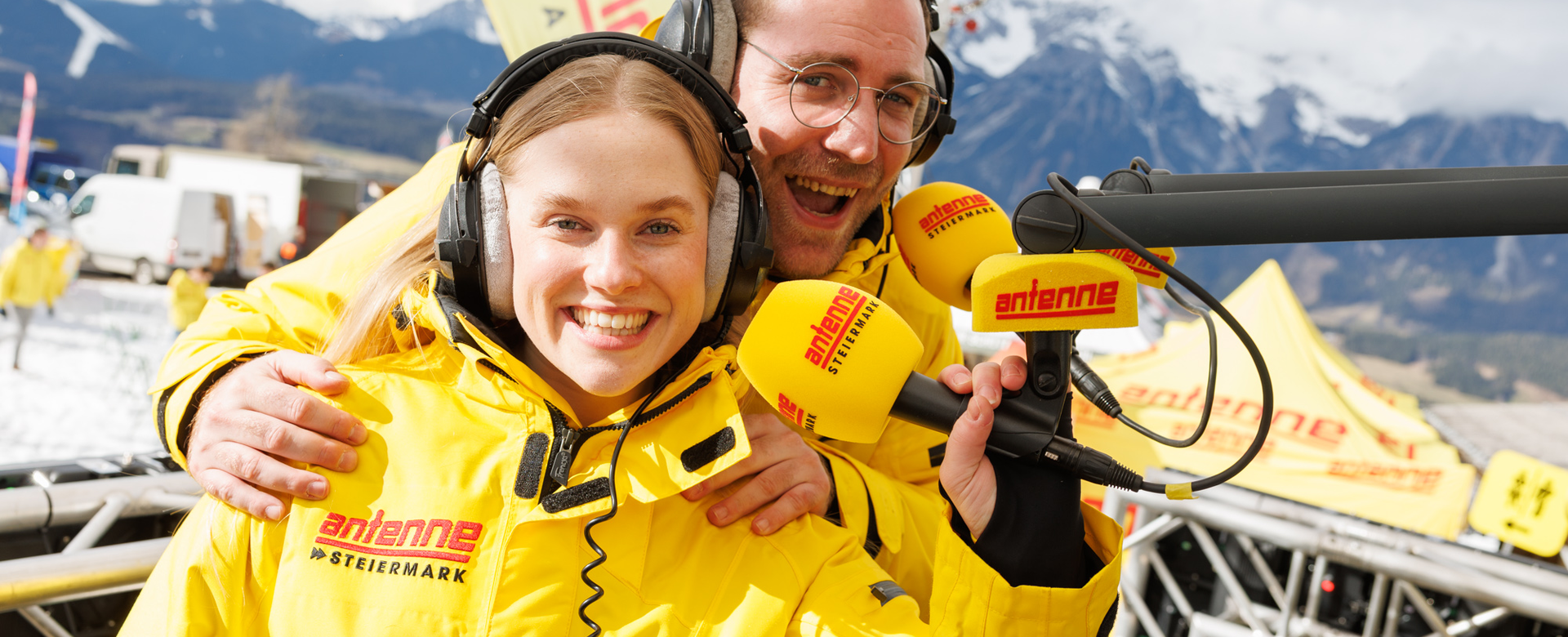 Zwei fröhliche Radiomoderatoren mit Headsets senden live vom Antenne Snowday auf der Planai. | © Erwin Scheriau