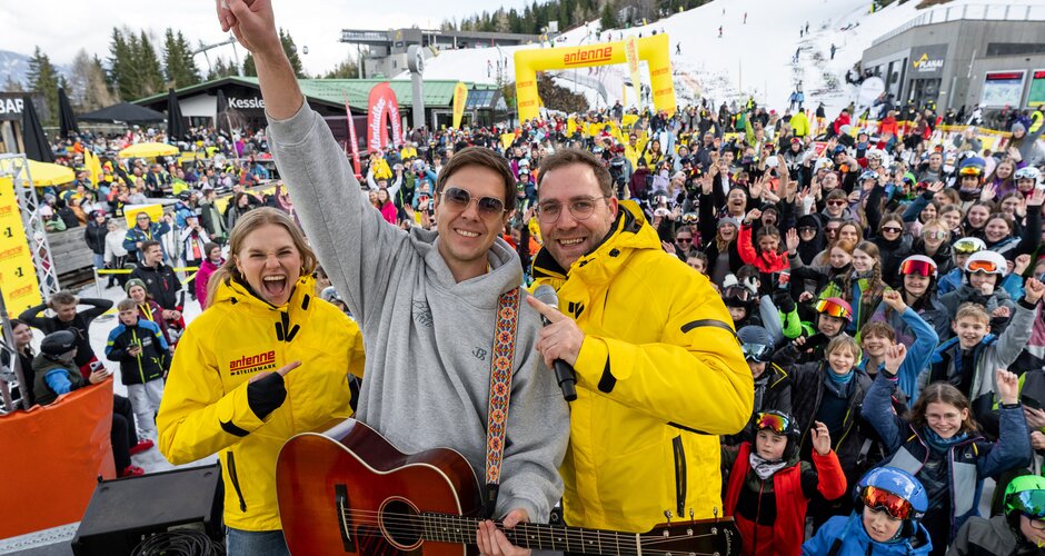 Musiker mit Gitarre und zwei Antenne-Moderatoren vor jubelndem Publikum im Schnee. | © Ripix