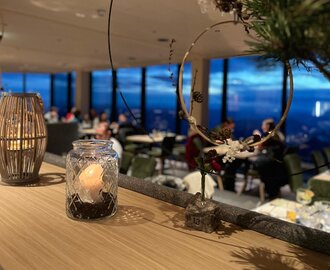 Adventstimmung am Dachstein bei Sonnenuntergang | © Planai-Hochwurzen-Bahnen Kerzendekoration im Glas vor Fenster mit Blick auf den Dachstein bei abendlicher Adventstimmung | © Planai-Hochwurzen-Bahnen