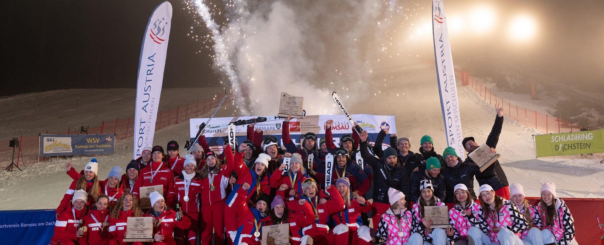 Große Siegergruppe posiert vor Feuerwerk und Bannern auf nächtlicher Skipiste | © Michael Simonlehner