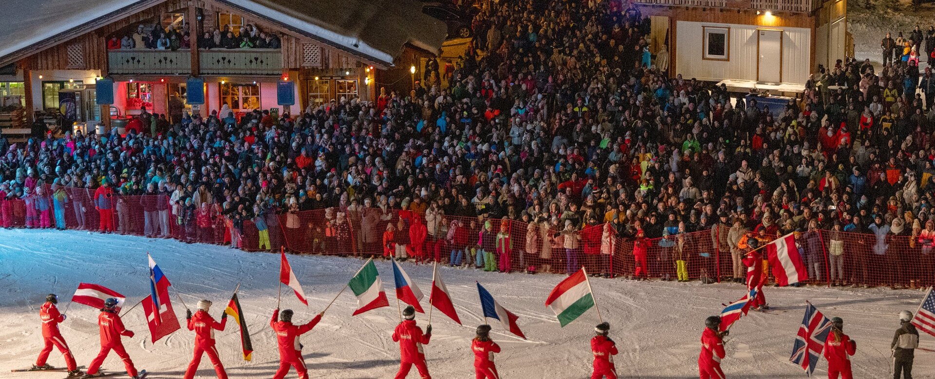 Skifahrer in Rot tragen Nationalflaggen vor großem Publikum bei Nacht auf der Piste | © Michael Simonlehner