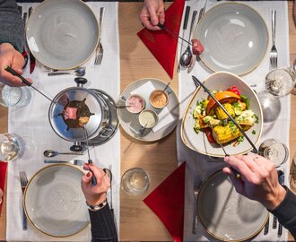 Fondueabend am Dachstein mit Fleisch, Gemüse und Saucen | © Martin Huber Vier Personen genießen Fleischfondue mit buntem Gemüse und Saucen an festlich gedecktem Tisch | © Martin Huber