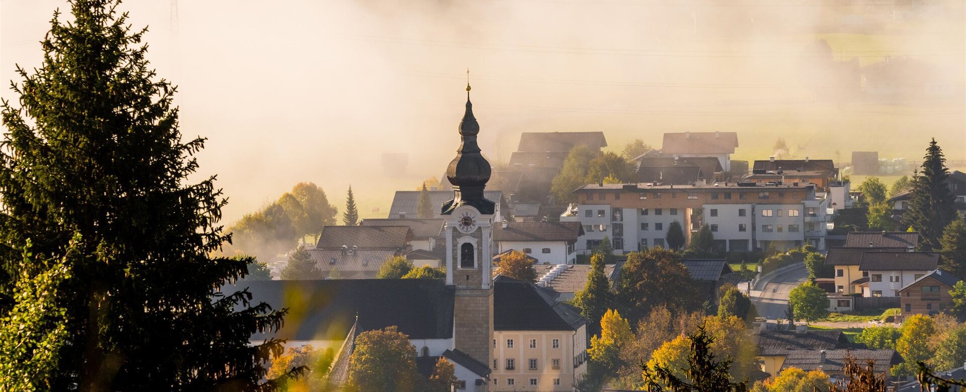 Nebliger Morgen in Altenmarkt mit Blick auf Kirchturm, herbstlich gefärbte Bäume und Häuser | © TVB Altenmarkt-Zauchensee