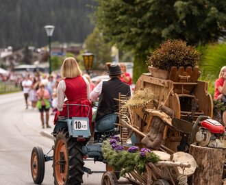 Ein Traktor mit traditionell gekleidetem Paar zieht einen alten Brauchtumskarren durch das Dorf beim Almabtrieb. | © ©bymichaelgroessinger_www.filzmoos.at