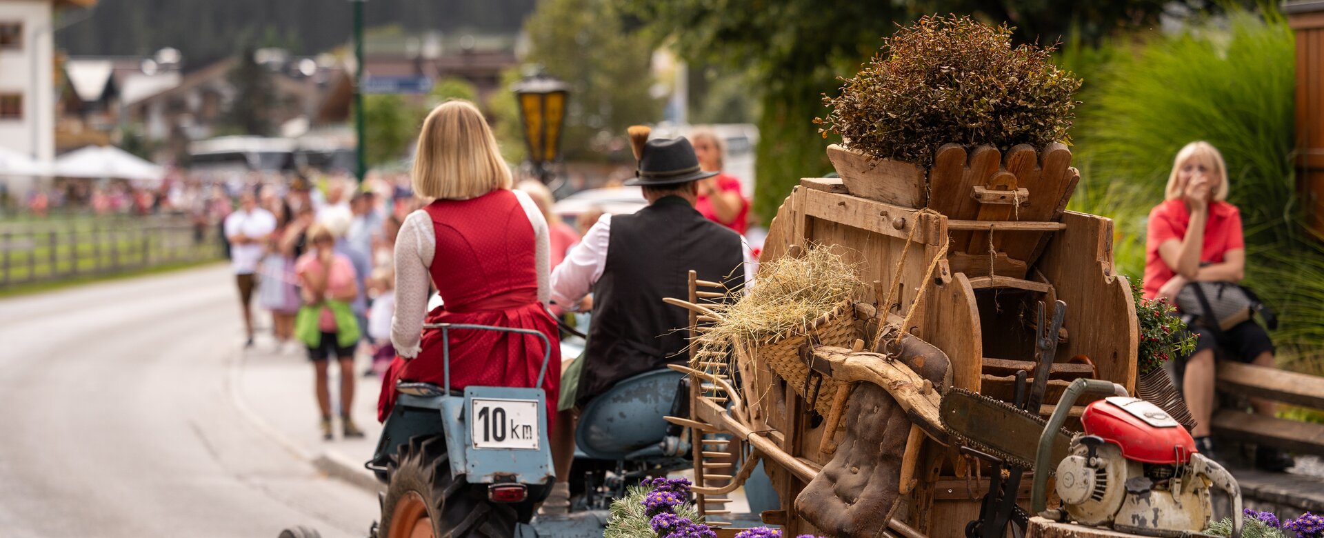 Ein Traktor mit traditionell gekleidetem Paar zieht einen alten Brauchtumskarren durch das Dorf beim Almabtrieb. | © ©bymichaelgroessinger_www.filzmoos.at