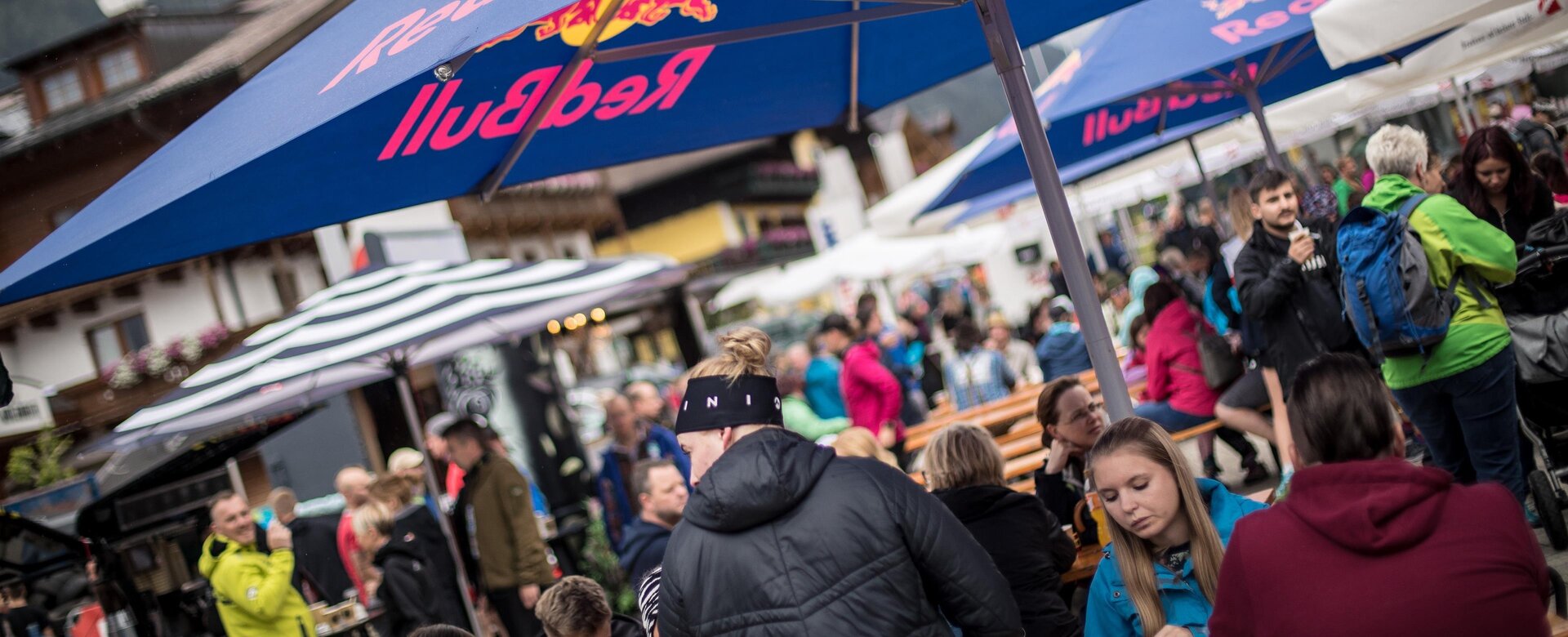 Viele Menschen sitzen und stehen unter Schirmen beim Gassenfest in Flachau | © Flachau Tourismus
