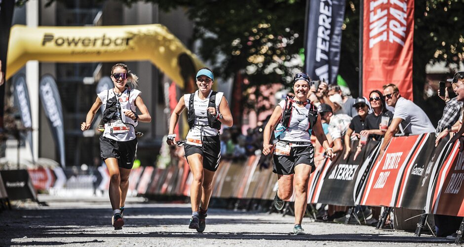 Drei Trailrunnerinnen laufen gemeinsam beim Zieleinlauf der adidas INFINITE TRAILS, jubelndes Publikum im Hintergrund | © Gasteinertal Tourismus GmbH, Sportograf