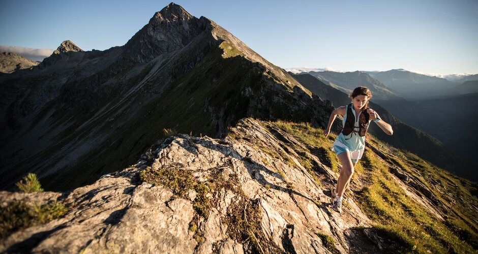 Sportlerin beim Trailrunning auf felsigem Gratweg mit Sonnenlicht und beeindruckender Berglandschaft im Hintergrund | © Gasteinertal Tourismus GmbH, Michael Mueller