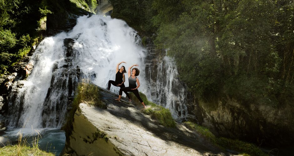 Zwei Frauen stehen auf einem Felsen in einer Yogapose und im Hintergrund ist ein Wasserfall | © Gasteinertal Tourismus GmbH, Marktl Photography