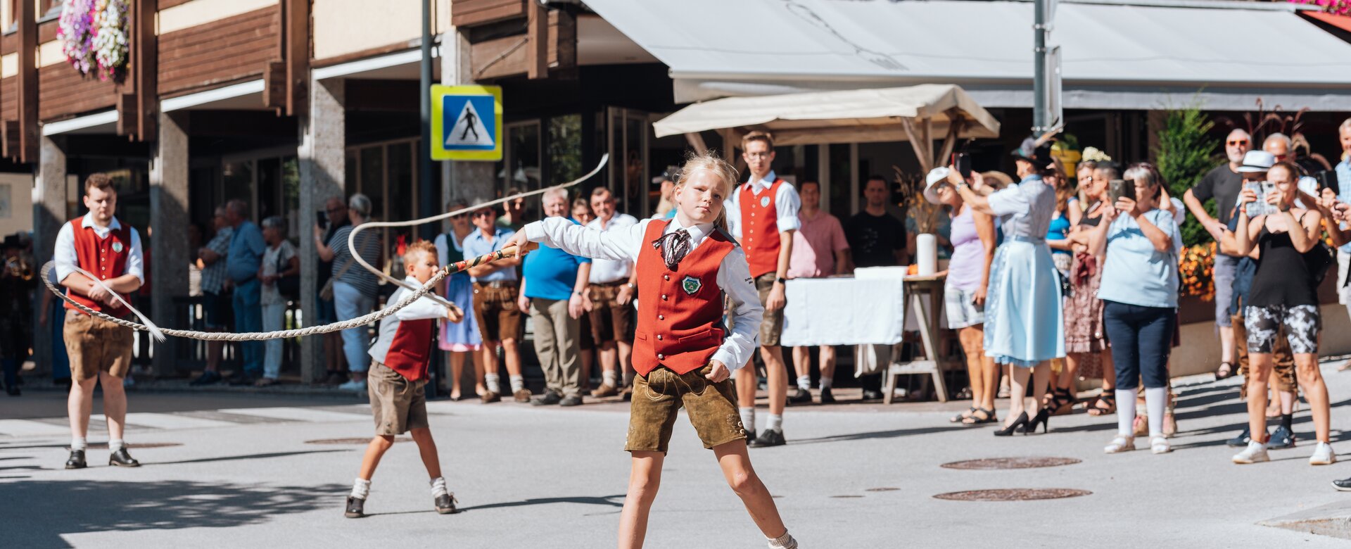 Children in traditional dress perform whip cracking, watched by a crowd at Maria Alm Harvest Festival. | © Miriam Lottes