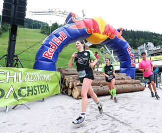 Mehrere Läufer überwinden ein Hindernis aus Baumstämmen unter dem Red-Bull-Bogen beim Tauern Circle in Schladming. | © David Geieregger
