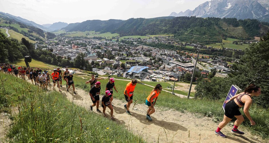 Läufer erklimmen einen steilen Hügel mit Blick auf Schladming und das Dachsteinmassiv beim Tauern Circle. | © Jasmin Walter