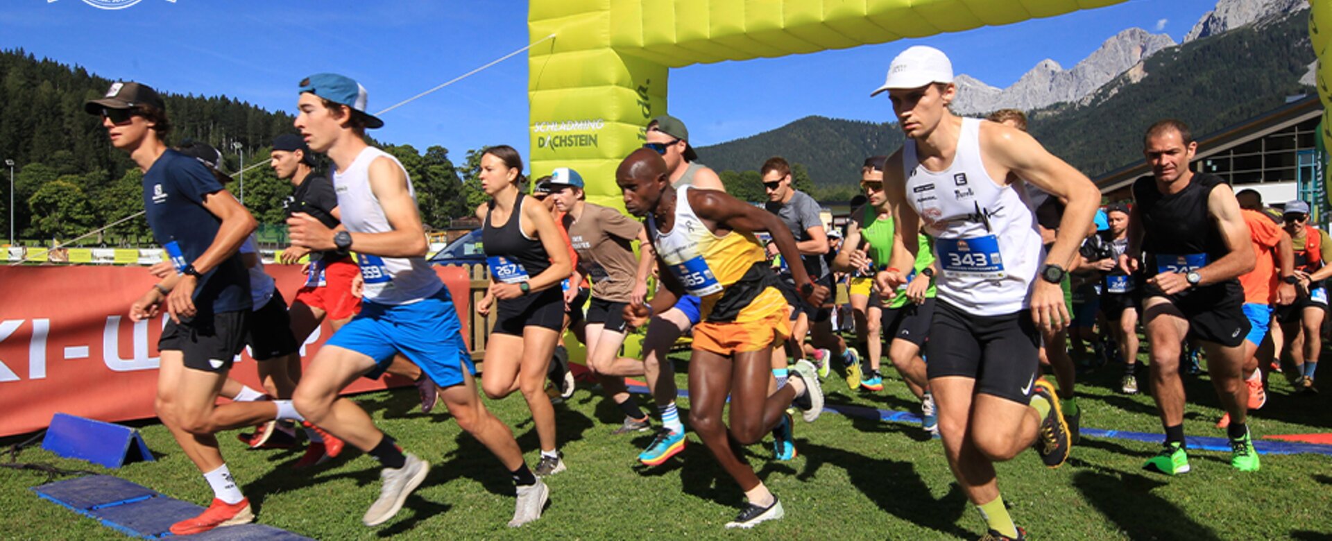 Runners start at Torlauf Dachstein under green arch with "Schladming" label, mountains and blue sky in the background | © Hans Simonlehner