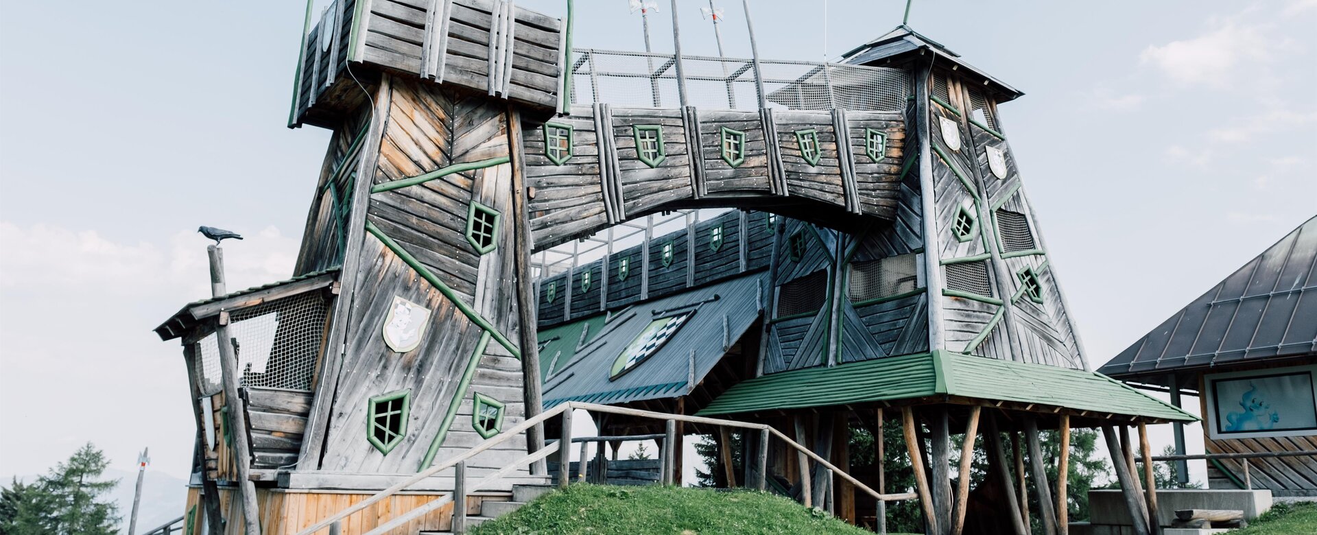 Schräge Holzfestung mit Brücke und Türmchen am Geisterberg, grüne Fensterläden, rote Fahne weht im Wind | © JOSalzburg