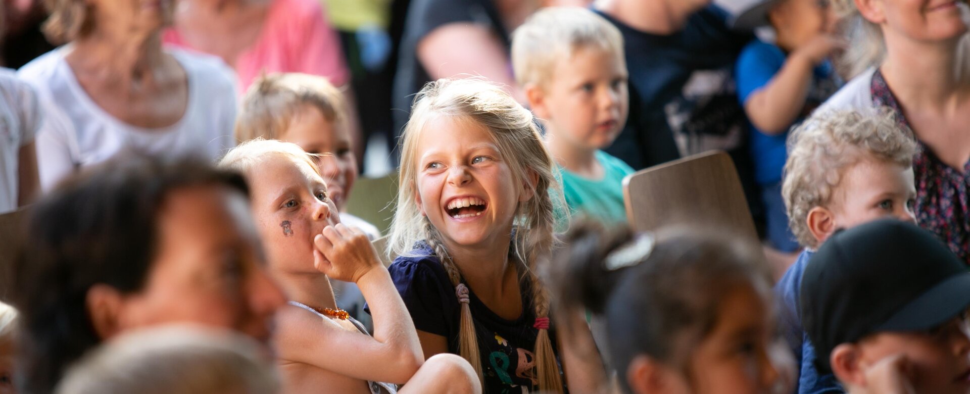 Happy children laughing in audience at JoKiWo & okidoki event, adults watching in the background | © JOSalzburg
