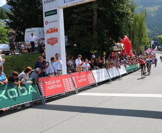 Radrennfahrer erreichen das Ziel der Tour of Austria, Zuschauer jubeln am Straßenrand unter dem Zielbogen | © JOSalzburg