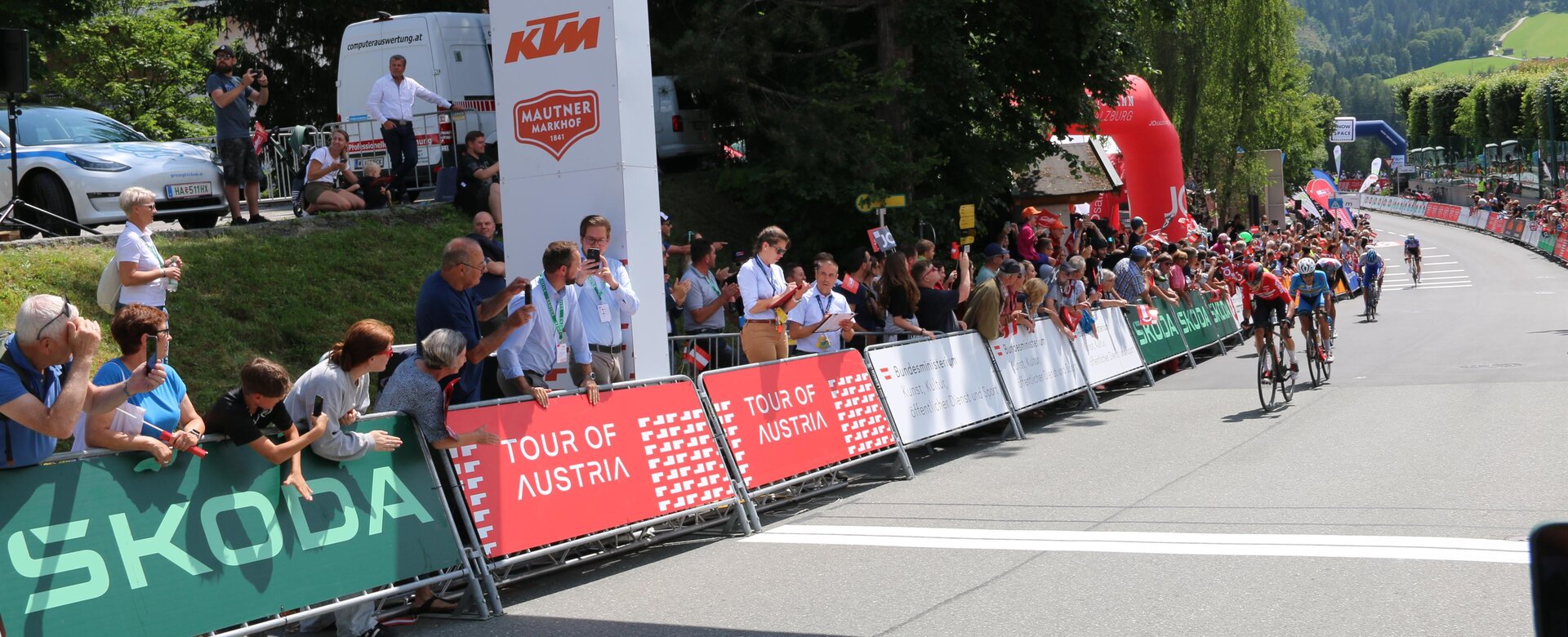 Radrennfahrer erreichen das Ziel der Tour of Austria, Zuschauer jubeln am Straßenrand unter dem Zielbogen | © JOSalzburg
