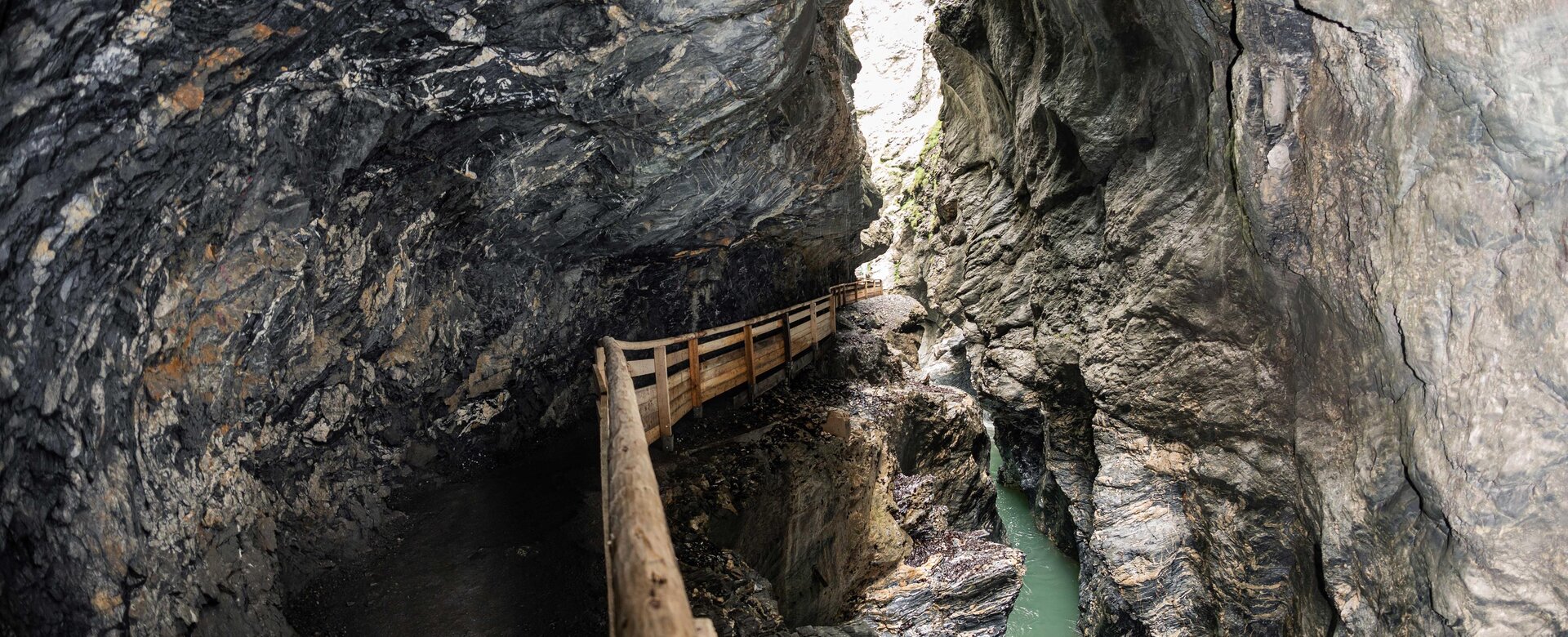 Holzsteg führt durch enge, felsige Schlucht mit grünem Wasser in der Liechtensteinklamm, Licht von oben | © JOSalzburg