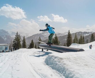 Skier balancing on rail in sunny snow park with snowy alpine mountains in background | © Shuttleberg / Absolut Park