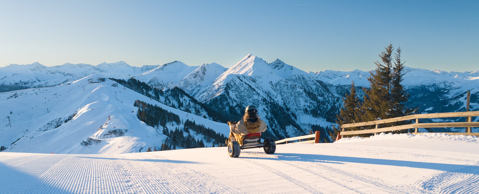 Person fährt Schneekart auf frisch präparierter Piste mit Blick auf verschneite Berge bei Sonnenschein. | © Dorfgasteiner Bergbahnen AG