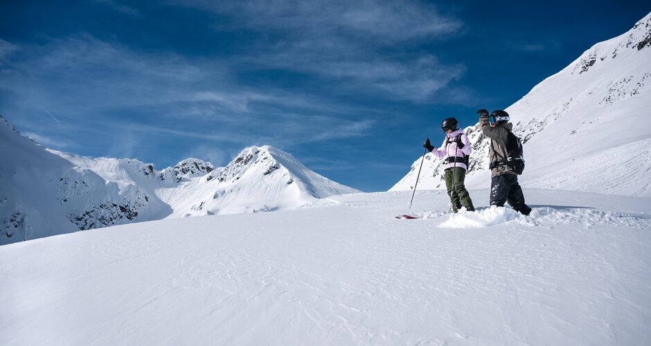 Zwei Freerider mit Helm und Rucksack stehen im Tiefschnee mit Blick auf verschneite Berggipfel | © Liftgesellschaft Zauchensee/C.Schartner