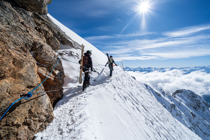 Approach to the Edelgrieß freeride route on sunny Dachstein | © Josh Absenger Two skiers with gear hike secured along a ridge to Edelgrieß freeride route | © Josh Absenger