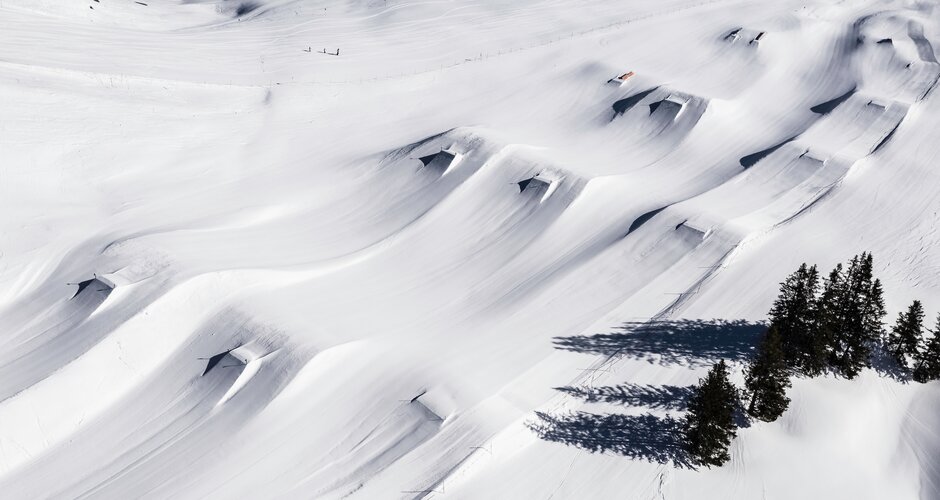 Drohnenbild des Kings Park Hochkönig mit frischem Powder, geshapten Kickern, Rails und markanten Baumschatten im Schnee.