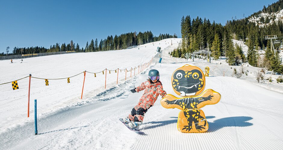 Child snowboarding in sunshine past colorful figure on Funslope at Shuttleberg ski resort area | © Shuttleberg