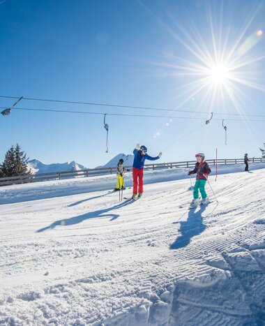 Familie fährt mit den Skiern eine Hügelpiste hinab und im Hintergrund ist ein Tellerlift | © Tourismusverband Großarltal