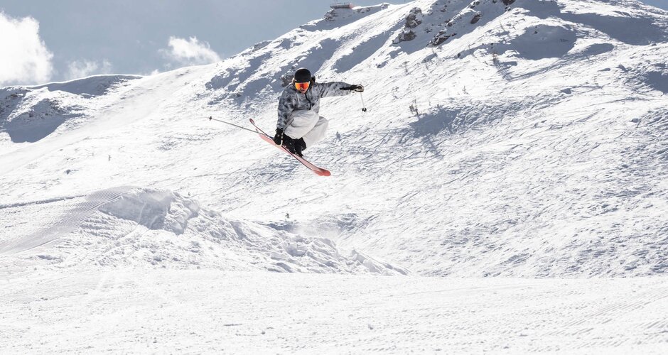 Skifahrer ist gerade in der Luft und berührt mit deiner rechten Hand den Ski | © Q-Parks Hannes Mautner