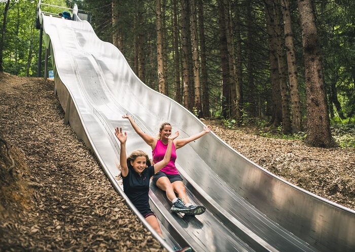 Forest fun: double slide action at Natrun adventure park Girl and woman laughing with raised arms while sliding down the twin slide at the forest slide park Natrun.