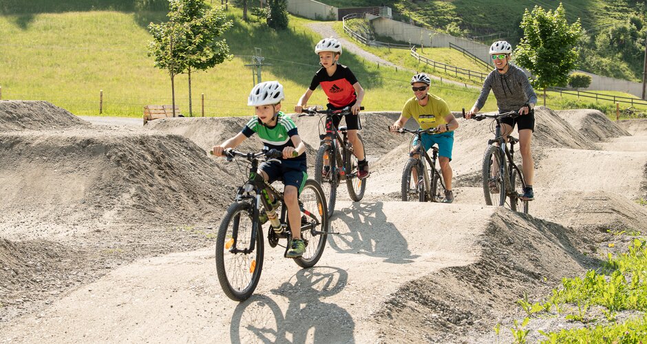 Zwei Kinder und zwei Erwachsene fahren mit Helmen am Pumptrack Dorfgastein über Wellen und Kurven | © Gasteinertal Tourismus GmbH, Fotoatelier Wolkersdorfer