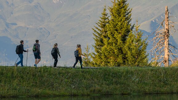 Vier Wanderer gehen am ruhigen Bergsee entlang mit Spiegelung und Bergen im Hintergrund | © Dorfgasteiner Bergbahnen AG