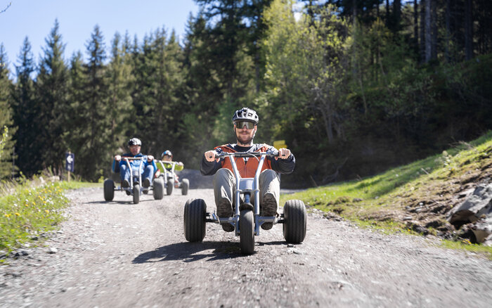 Adrenalingeladene Mountaincart-Abfahrt durch den Wald | © Dorfgasteiner Bergbahnen AG Gruppe fährt mit Mountaincarts rasant bergab auf Schotterweg durch Waldgebie | © Dorfgasteiner Bergbahnen AG