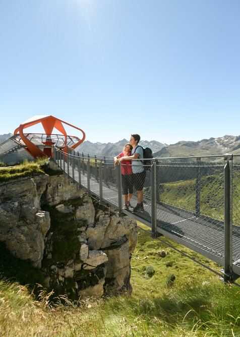 Zwei Personen genießen auf dem Felsenweg am Stubnerkogel die Aussicht zur Glocknerblick-Plattform bei strahlendem Wetter | © Gasteiner Bergbahnen, Marktl Photography