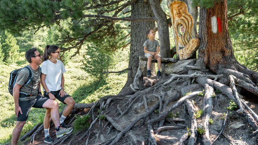 Familie am Graukogel beim geschnitzten Zirbengeist auf Wurzelbank im Wald | © Skigastein, seven frames
