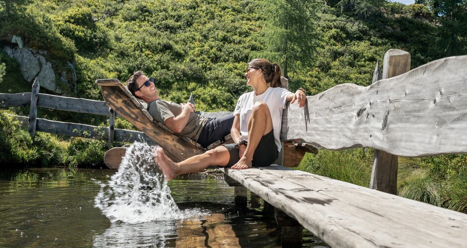 Paar entspannt auf Holzliegen und kühlt die Füße im Wasser am Graukogel | © Skigastein, seven frames