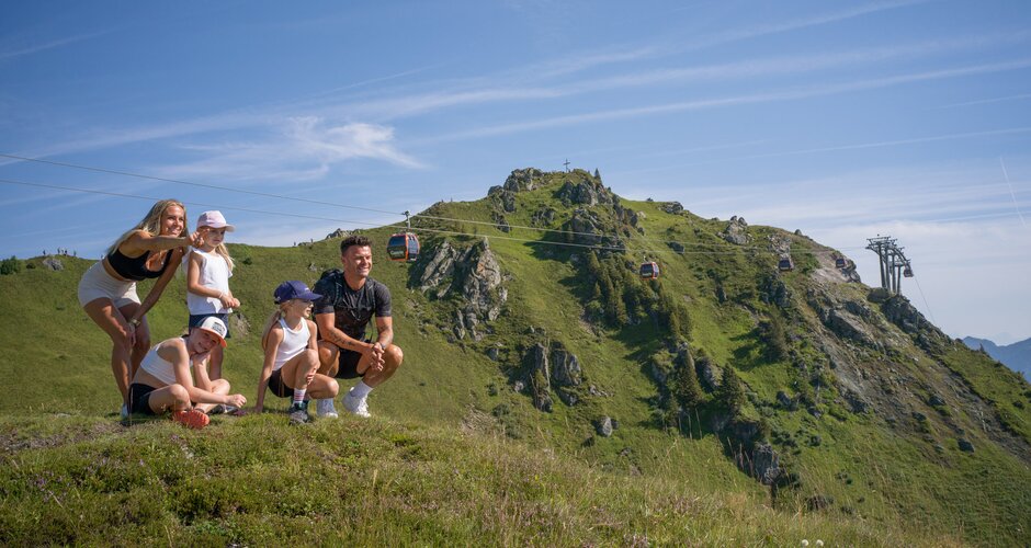 Familie mit drei Kindern rastet auf Wiese der Schlossalm in Gastein und blickt auf Berge und Seilbahn | © Balazs Kovacs