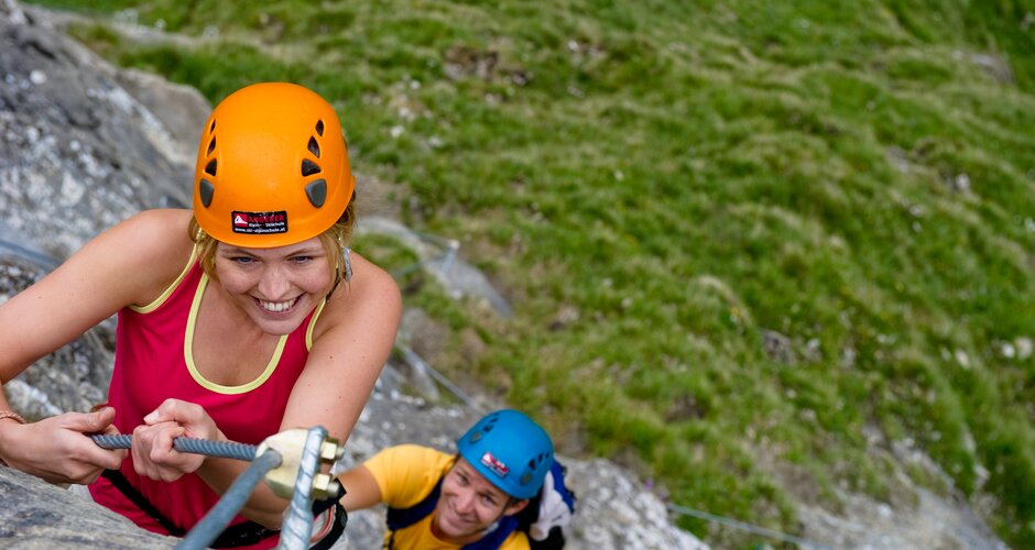 Smiling woman climbs secured via ferrata at Schlossalm, followed by second climber with helmet and harness | © Gasteiner Bergbahnen AG, Claudia Ziegler
